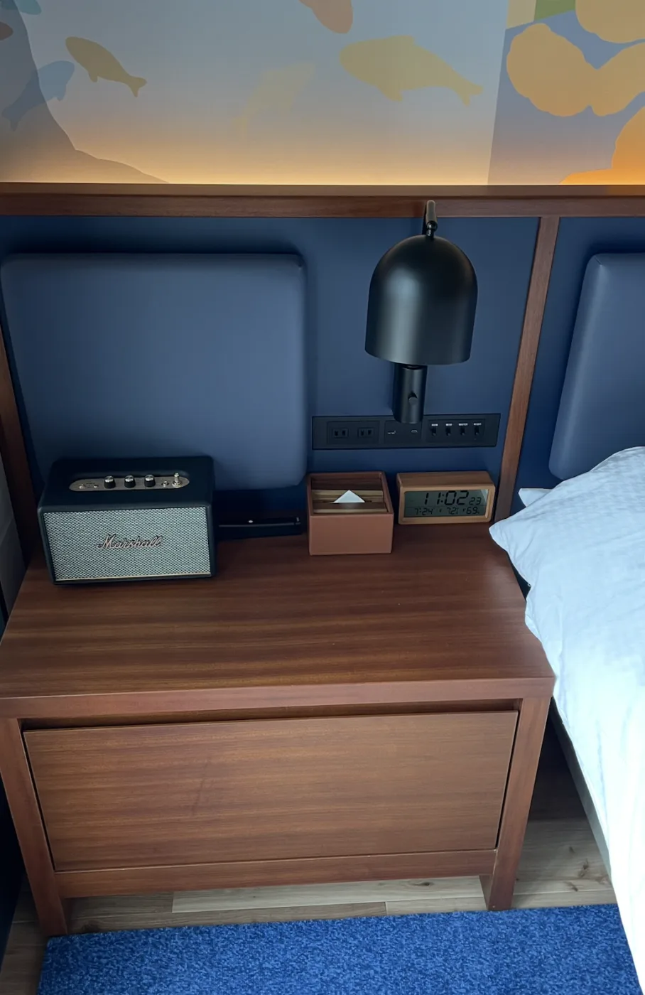 Warm concealed light glowing behind a padded headboard, with a bedside tray and clock