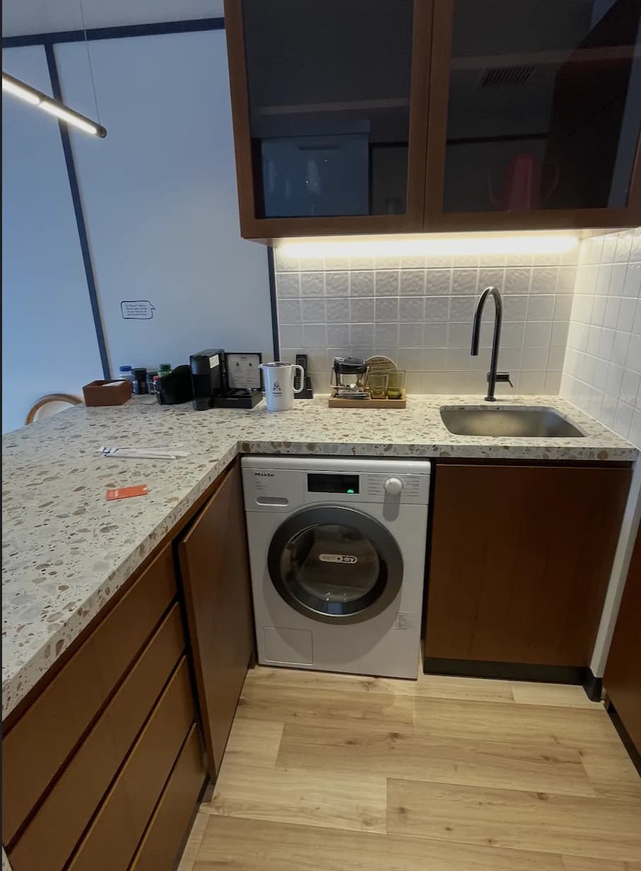 An in-room kitchenette with a warm under-cabinet light strip, a coffee and tea setup, and a gooseneck tap